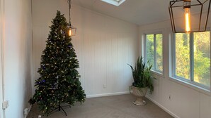 Una habitación con un árbol de Navidad, una planta en maceta y una ventana con vistas a árboles.