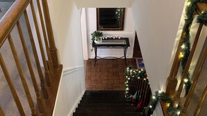Una escalera de madera con barandilla negra, que lleva a un rellano con una mesa pequeña y un ventanal.