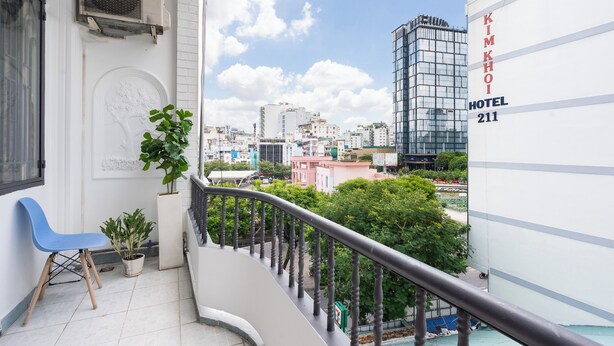 A balcony with a blue chair, potted plants, and a view of the cityscape including the Kimkhoi Hotel 211. - Phan Hotel (Ho Chi Minh City)