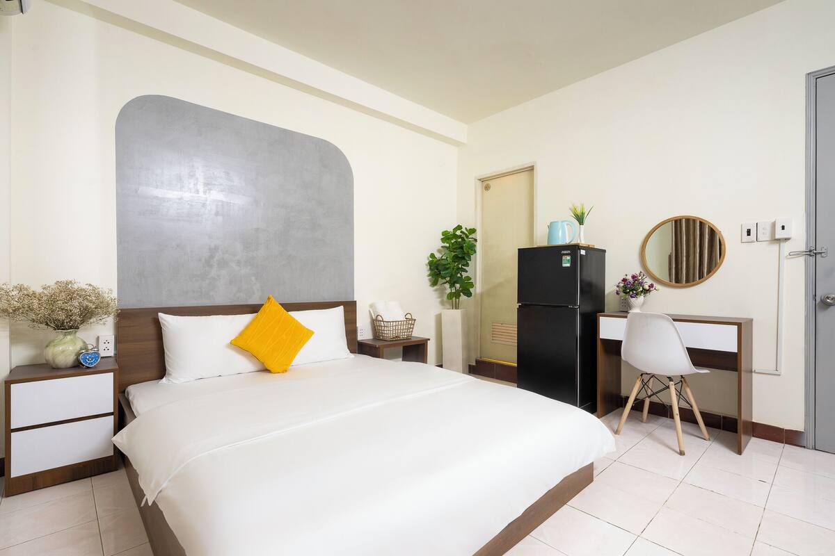 Een hotelkamer met een groot bed, een bureau met stoel, een koelkast, een spiegel en een deur.