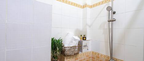 Ein Badezimmer mit weißen und orangefarbenen Fliesen, einer Dusche, einem Handtuchhalter, einer Topfpflanze und Pflegeprodukten.