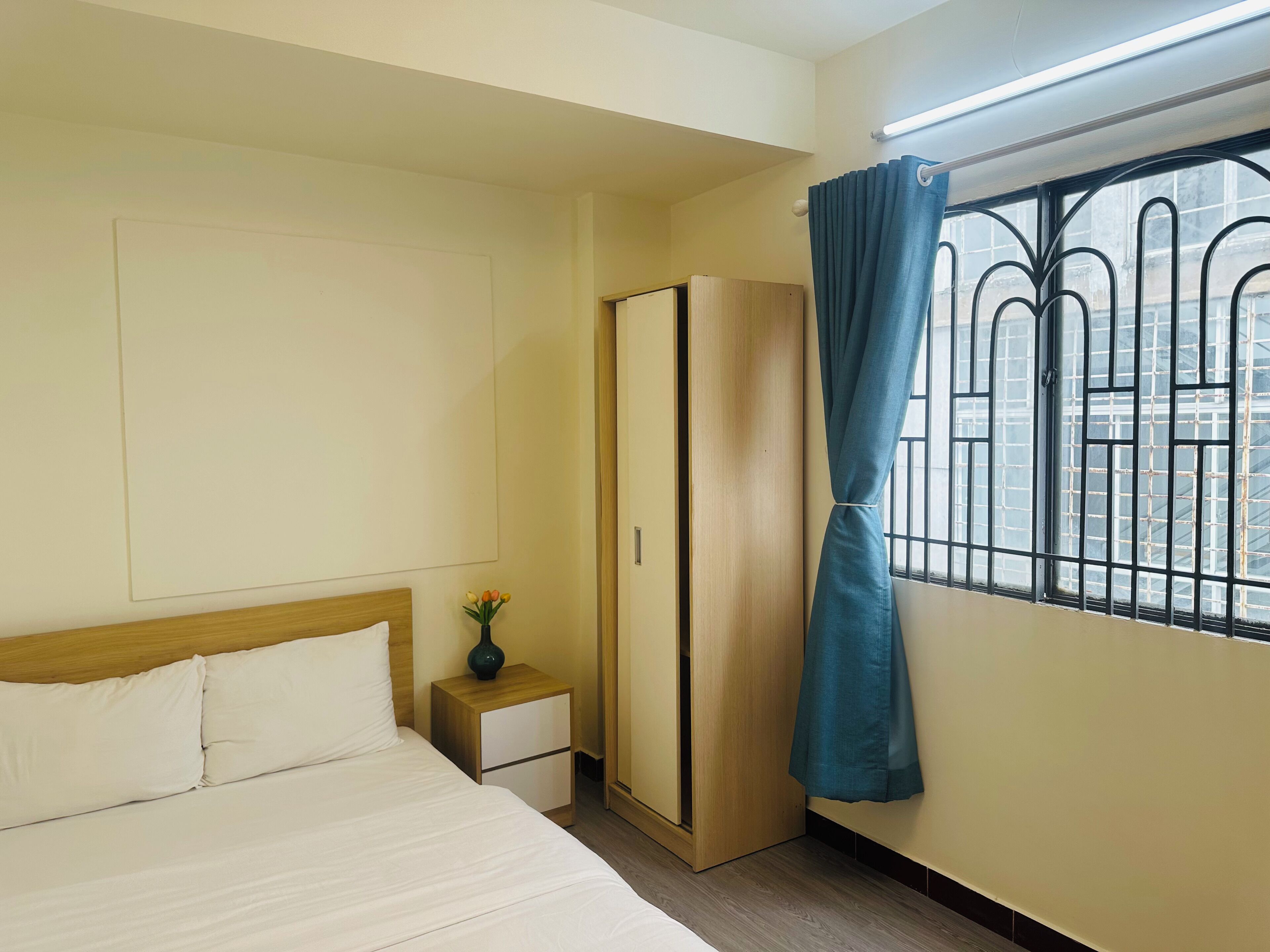A hotel room with a bed, a nightstand, a wardrobe, and a window with a curtain.