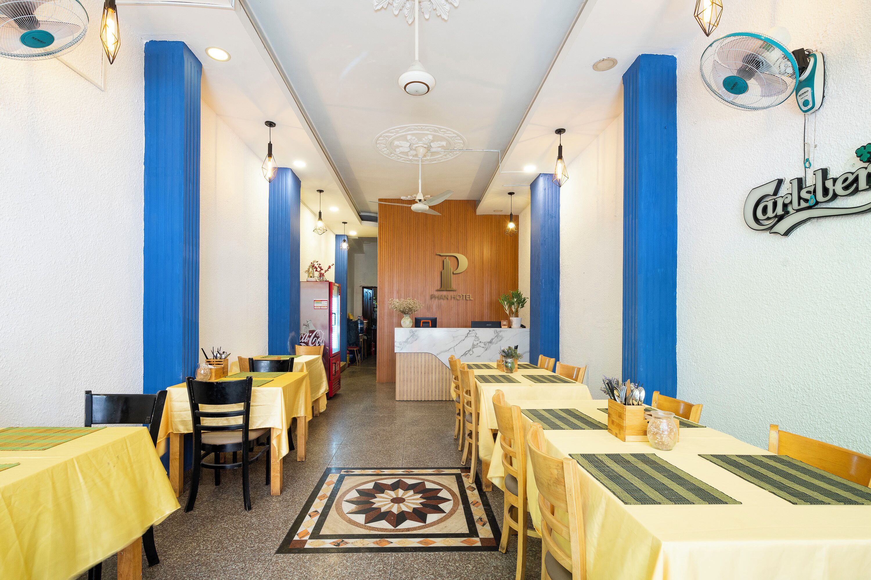Un restaurant avec des tables jaunes et des touches de bleu, un comptoir en marbre et un ventilateur de plafond.