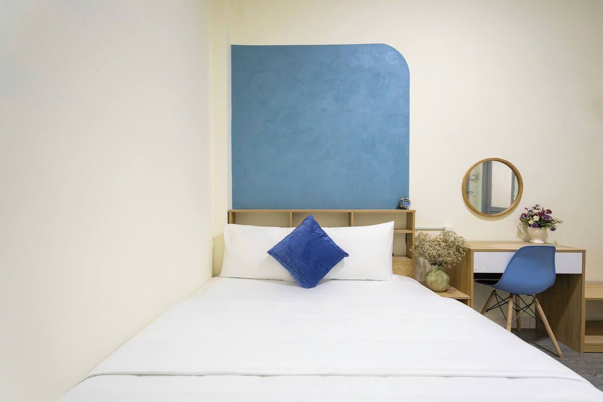 Een hotelkamer met een bed, een bureau, een stoel, een spiegel en een vaas met bloemen.