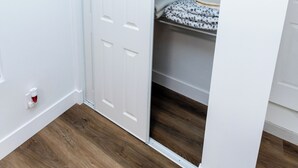 Een kamer met een houten vloer, een witte deur en een kast met hangende kleding.