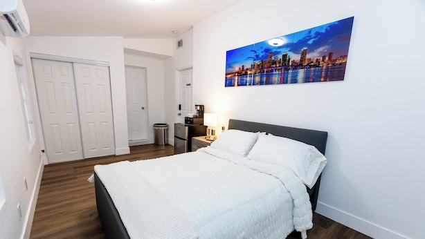 Een netjes ingerichte slaapkamer met een bed, nachtkastje, lamp en een stadsgezicht schilderij aan de muur.