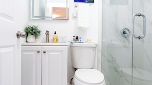 Een badkamer met een wit toilet, een douchecabine van glas, een marmeren vloer en een witte kast met een plant.