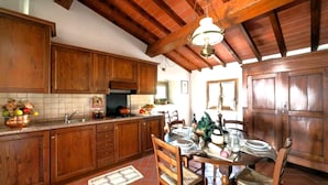 Una cocina con armarios de madera, salpicadero de azulejos, una mesa de comedor para cuatro personas y una lámpara colgante.