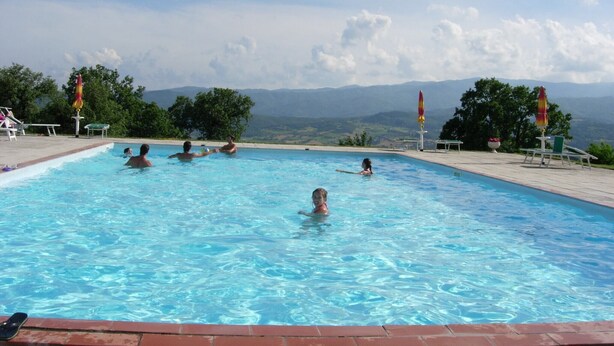 Una piscina con gente, rodeada de árboles y montañas al fondo.