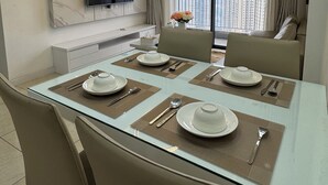 A modern dining area with a glass table, beige chairs, and a chandelier.