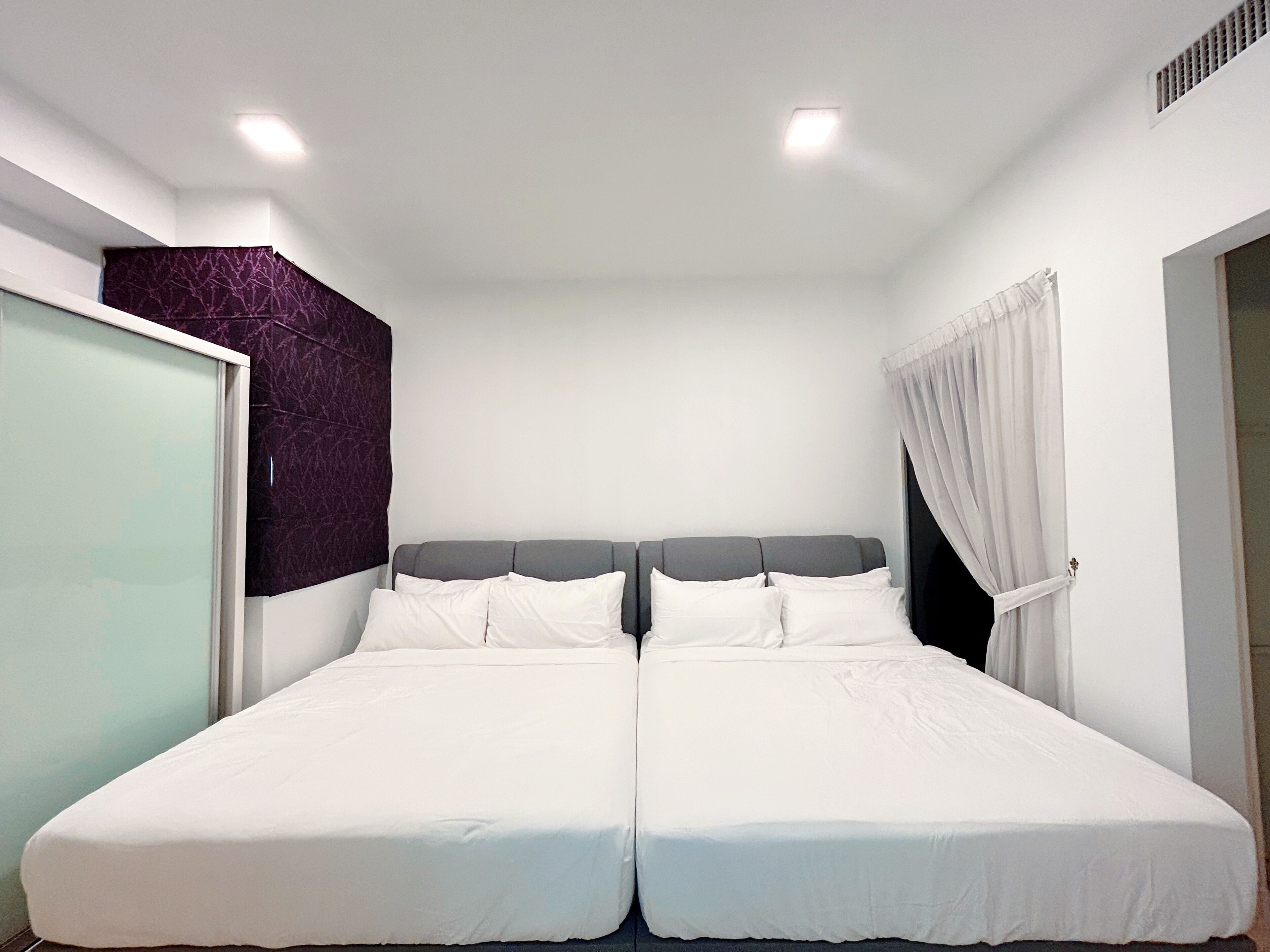 A double bed with white bedding in a room with white walls and a ceiling light.