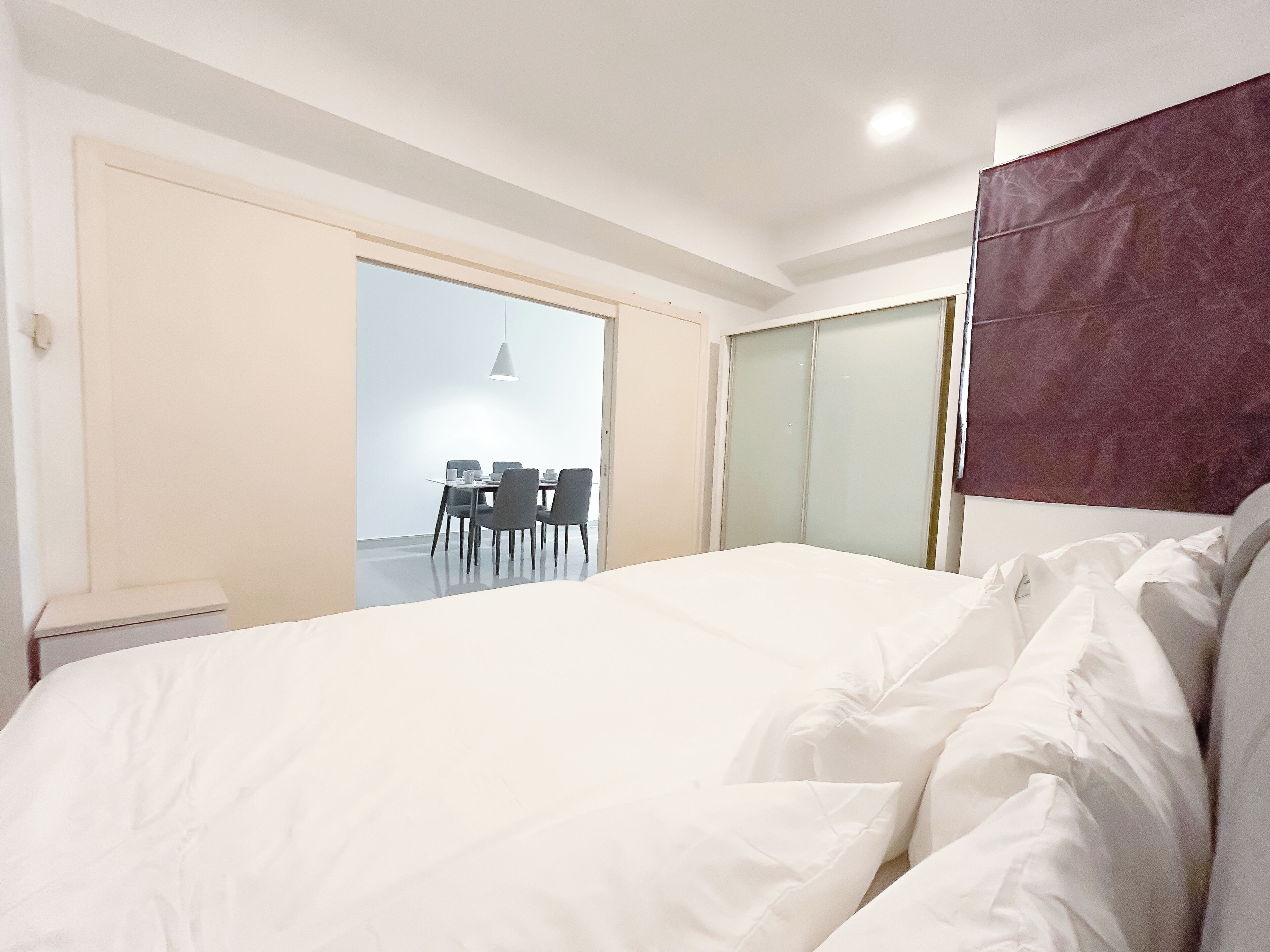 A bedroom with a large bed, a desk with chairs, and a sliding glass door leading to a balcony.