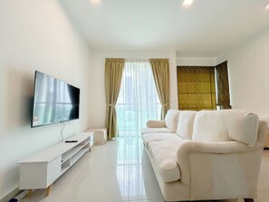 En moderne stue med et fladskærms-tv, en hvid sofa og et sofabord i glas.