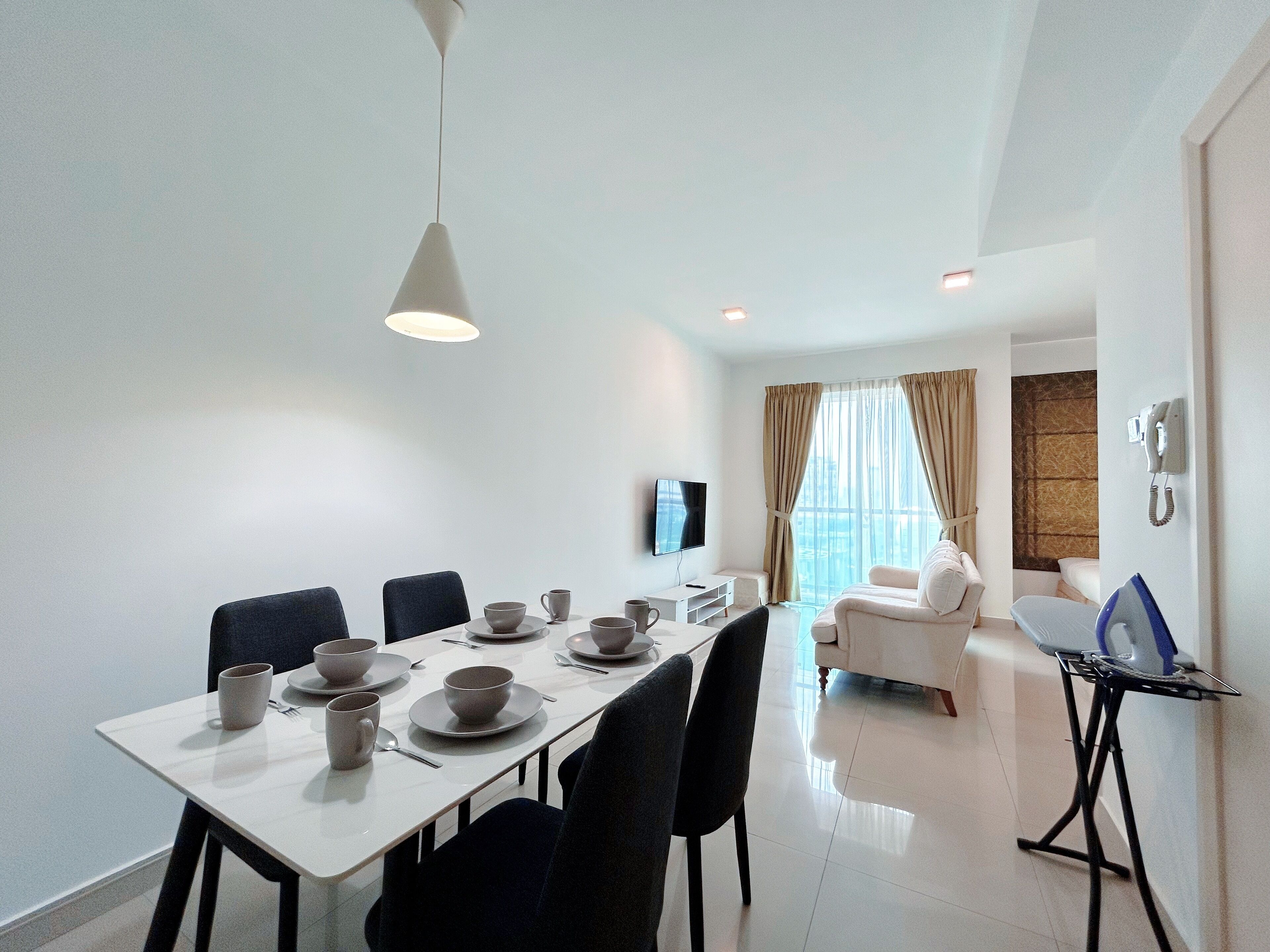 A modern hotel room with a dining area, a sofa, a TV, and a phone on the wall.