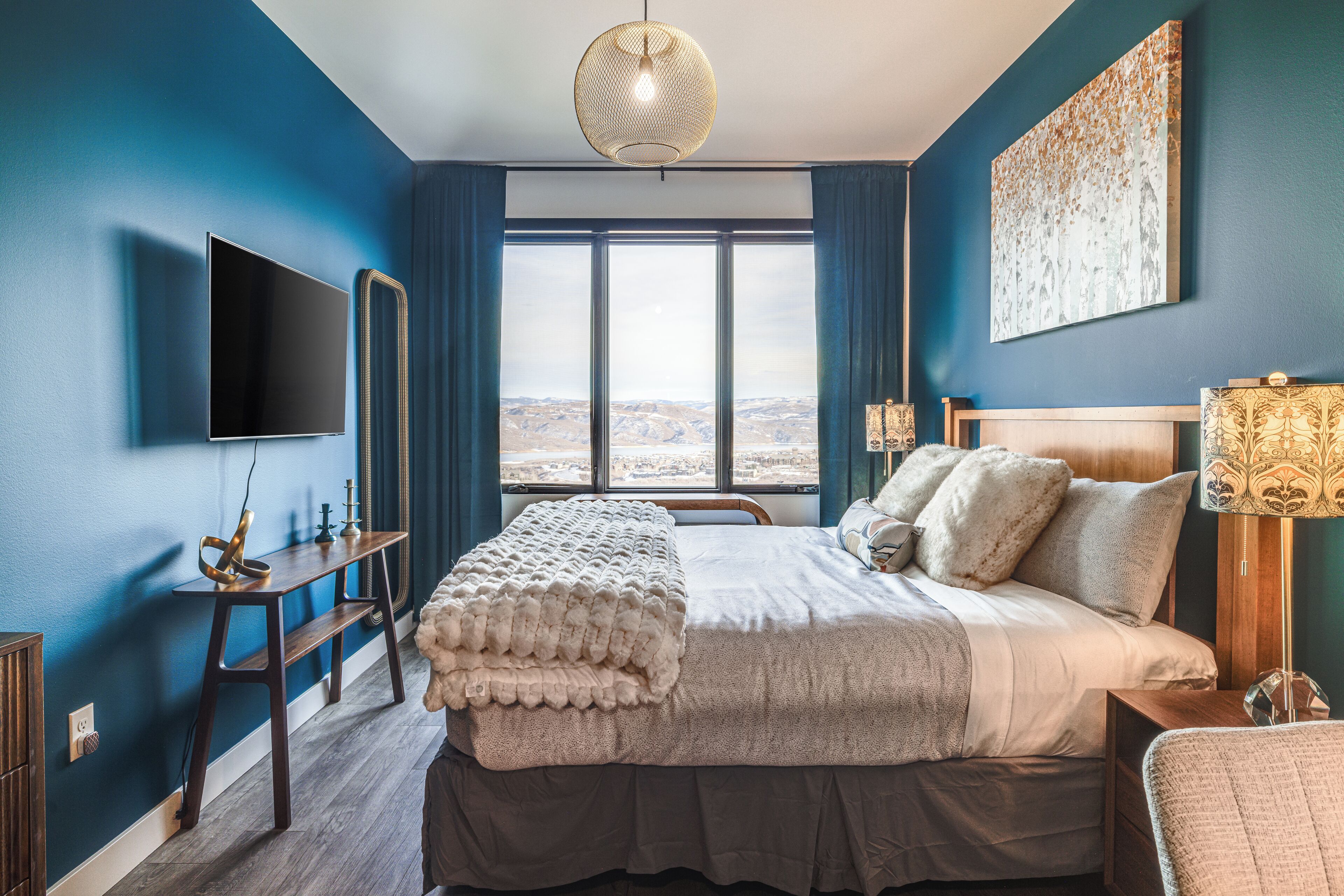 Un dormitorio moderno con una cama grande, un televisor de pantalla plana, una mesita de noche de madera y vistas al paisaje a través de la ventana.