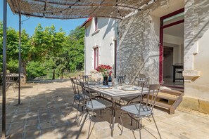 Eine Terrasse im Freien mit einem Essplatz, umgeben von StĂŒhlen, und einer Pergola darĂŒber.