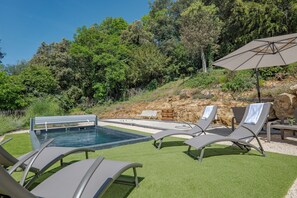 Ein Poolbereich mit LiegestĂŒhlen und Sonnenschirm, umgeben von GrĂŒnpflanzen und einer felsigen Böschung.