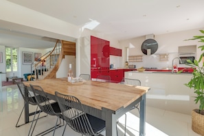 A modern kitchen with red cabinets, a wooden dining table with metal chairs, and a staircase leading to an upper level. - Salvibabette, a light and spacious holiday home in a gastronomic area (Vitrac)