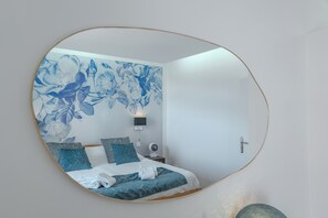 Ein Schlafzimmer mit Bett, Kissen, einem Nachttisch, einem an der Wand montierten Fernseher und einem Spiegel.
