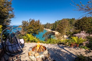 A fire pit with a view of a beach and forest. - Jacuzzi Suite - Ocean Views & Beach (Kaiteriteri)