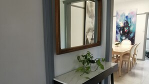 Ein Flur mit weißer Wand, einem spiegelnden Wandbild mit Holzrahmen, einem Marmorkonsolentisch mit Pflanze sowie einem Essbereich mit Tisch und Stühlen.