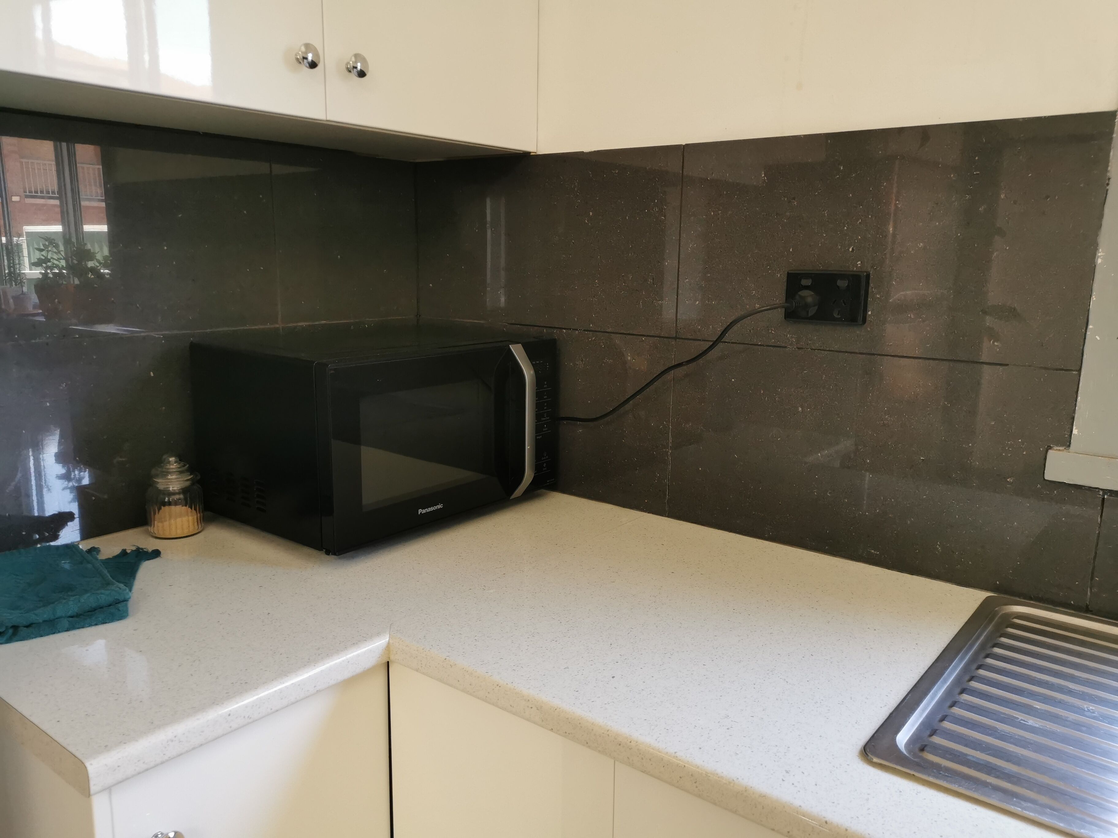 Een keuken met een zwarte magnetron, een klein glazen potje en een blauwgroene doek op het aanrecht.