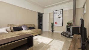 Ein modernes Wohnzimmer mit einem beigefarbenen Sofa, einem Flachbildfernseher, einem Kaminofen und einem 'Vogue 1950' Poster an der Wand.