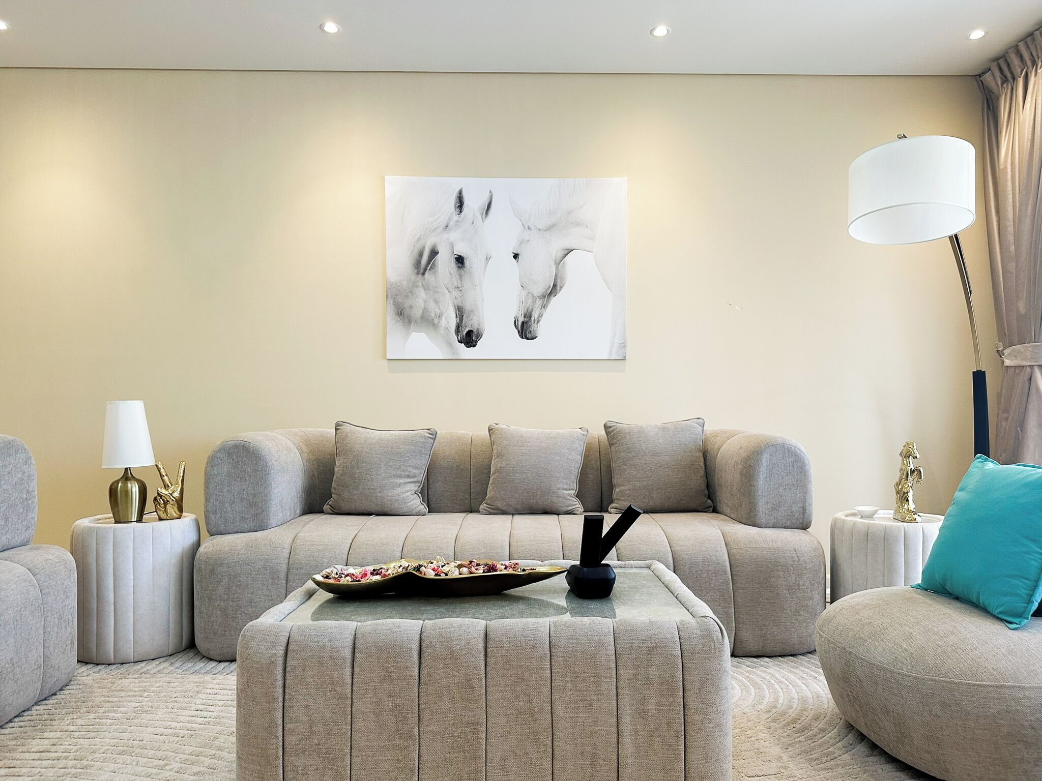 Una sala de estar moderna con un sofá beige, una mesa de centro y una obra de arte de caballos en la pared.