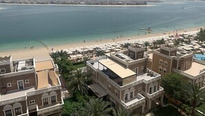 Un hôtel situé sur la côte, composé de plusieurs bâtiments, avec une plage et, en arrière-plan, la silhouette d’une ville.