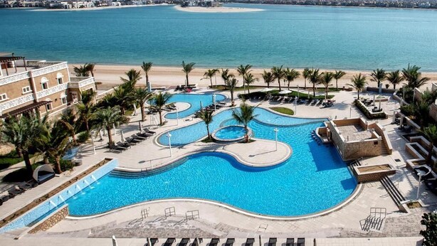 Une piscine d’hôtel comprenant plusieurs zones, des palmiers et offrant une vue sur la plage.