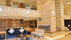 Un hall d’entrée spacieux avec un plafond haut, un comptoir de réception en marbre, un coin salon avec des canapés et une cheminée.
