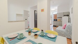 Un coin repas avec une table dressée pour quatre personnes, une cuisine en arrière-plan et un canapé à motifs.
