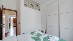 Une chambre d’hôtel avec un lit, une petite table, une armoire et un couloir menant à une autre pièce.