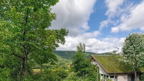 A house with a green roof, surrounded by lush greenery and hills in the background. - Apartment 'Burgblick' with Shared Garden and Wi-Fi (Bad Urach)