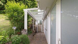 A covered outdoor pathway leading to a building entrance, surrounded by greenery and a stone-paved area. - Apartment 'Burgblick' with Shared Garden and Wi-Fi (Bad Urach)
