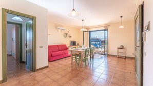 A spacious living area with a red sofa, dining table, and chairs. There is a TV and a small kitchen area visible.