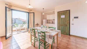 A dining area with a table set for four, a kitchen with white cabinets, and a sliding glass door leading to a balcony with outdoor furniture.