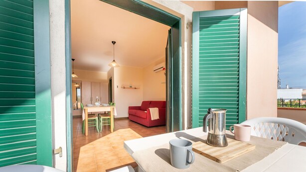A balcony with a table, chairs, a coffee pot, and a mug.