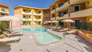 A pool area with lounge chairs and umbrellas, surrounded by multi-story buildings with balconies.