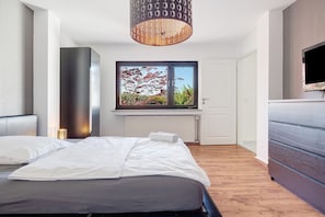Un dormitorio con cama, ventana con vistas a árboles, televisor y radiador.