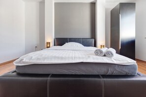 A modern hotel room with a large bed, a headboard, bedside lamps, and a wardrobe.