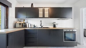 A modern kitchen with dark cabinets, a built-in oven, and a window with curtains.