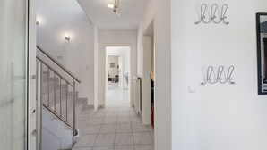 A hallway with a staircase, a light fixture, and wall-mounted hooks.