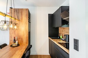 A modern kitchen with a wooden dining table, black cabinets, and pendant lighting. - Design Apartment with Shared Garden, Balcony, and Wi-Fi in Goslar (Goslar)