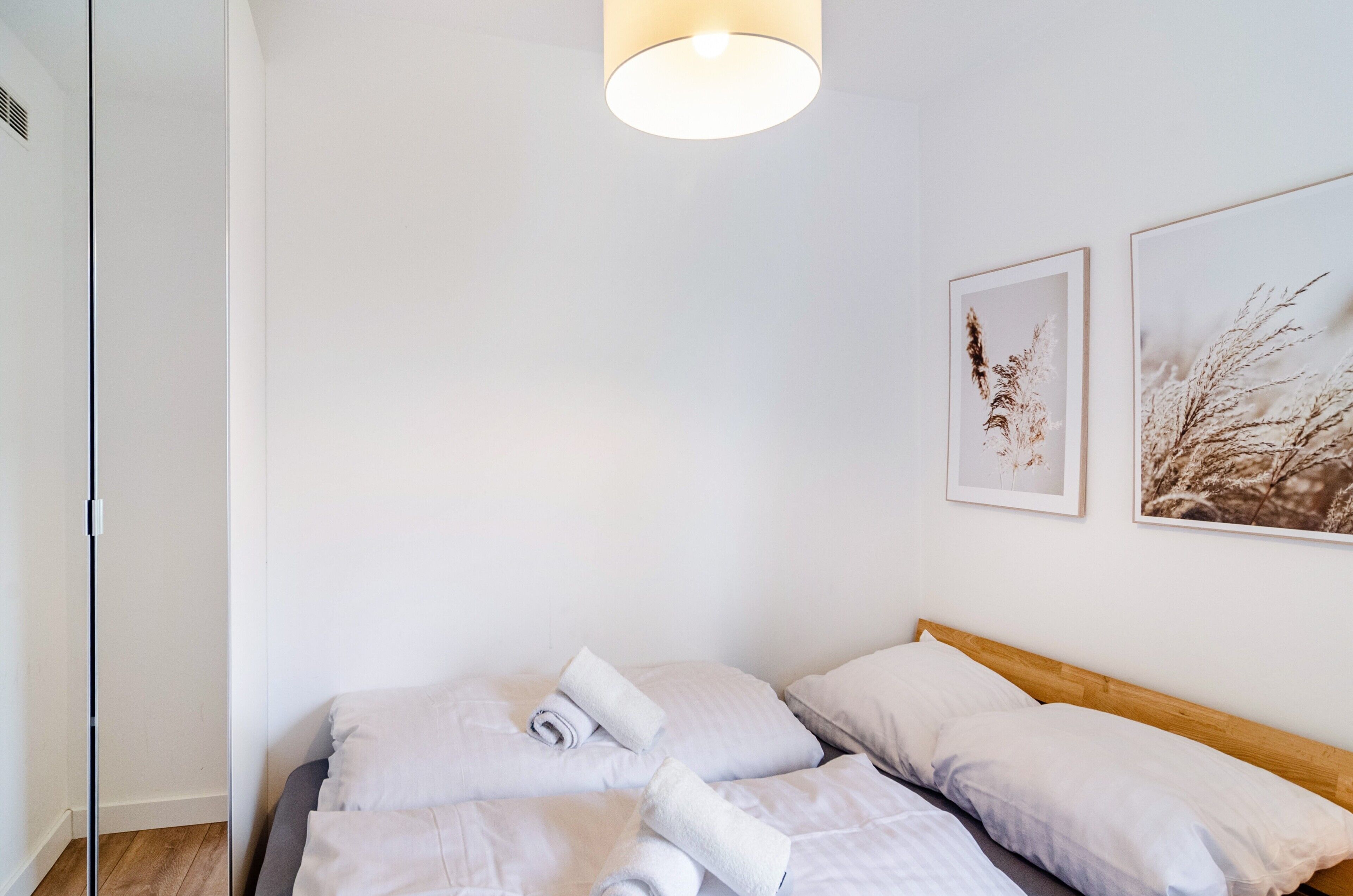 Un dormitorio con cabecera de madera, una cama con ropa blanca y dos láminas botánicas enmarcadas en la pared.
