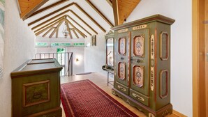 A room with wooden beams, a green cabinet with intricate designs, a red patterned rug, and a view of a balcony.