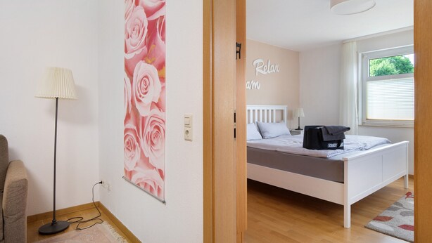 A bedroom with a bed, a wall with a 'Relax' sign, a window with blinds, and a floor lamp. - Apartment 'Ermstal' with Shared Garden and Wi-Fi (Bad Urach)