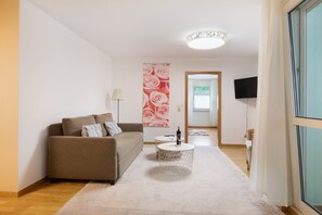 Un salon avec un canapé, une table basse ronde, une lampe, un téléviseur et une grande fenêtre.