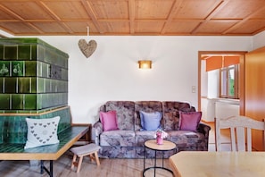 Une pièce avec un plafond en bois, un banc recouvert de carreaux verts, un canapé à motifs, une petite table ronde et une chaise en bois.