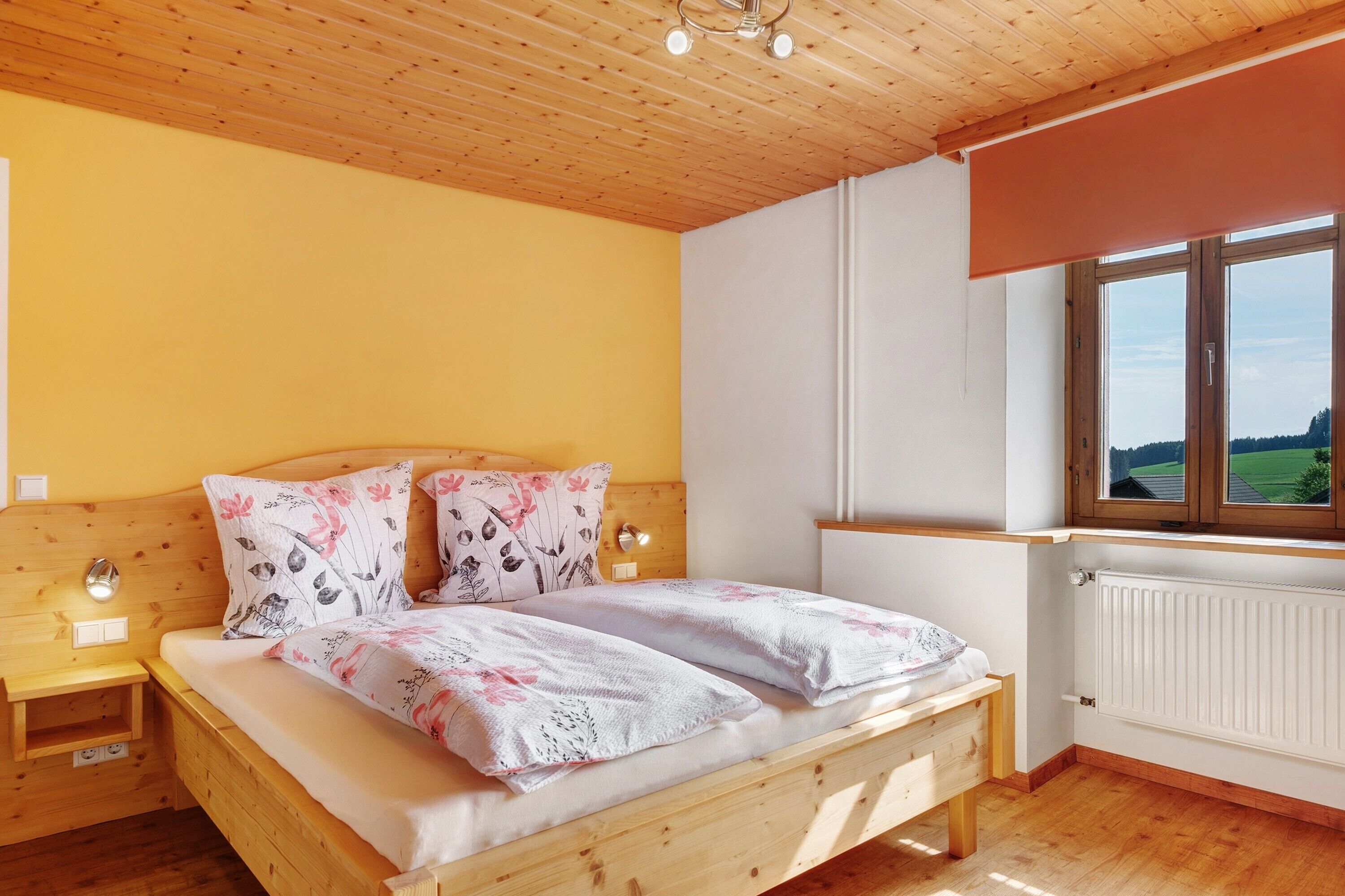 A wooden bed with floral bedding, a nightstand, a window with a view, and a white radiator.